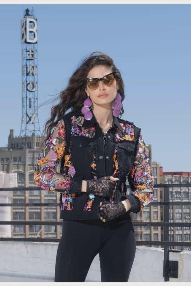 Woman wearing a colorful sequin embroidered floral black jacket on a rooftop with cityscape background