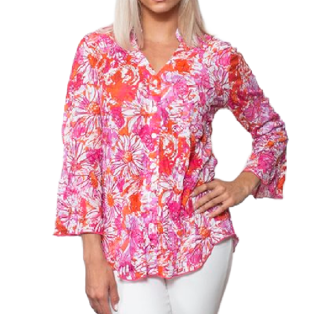 A woman modeling a vibrant pink, orange, and white floral long-sleeve blouse with white pants, set against a plain white background.