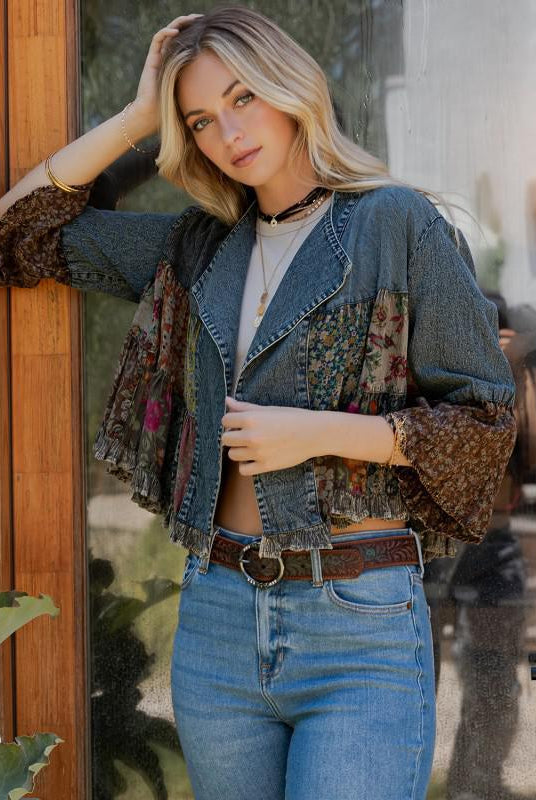 Woman wearing a denim jacket over a patterned shirt with high-waisted jeans, standing indoors.