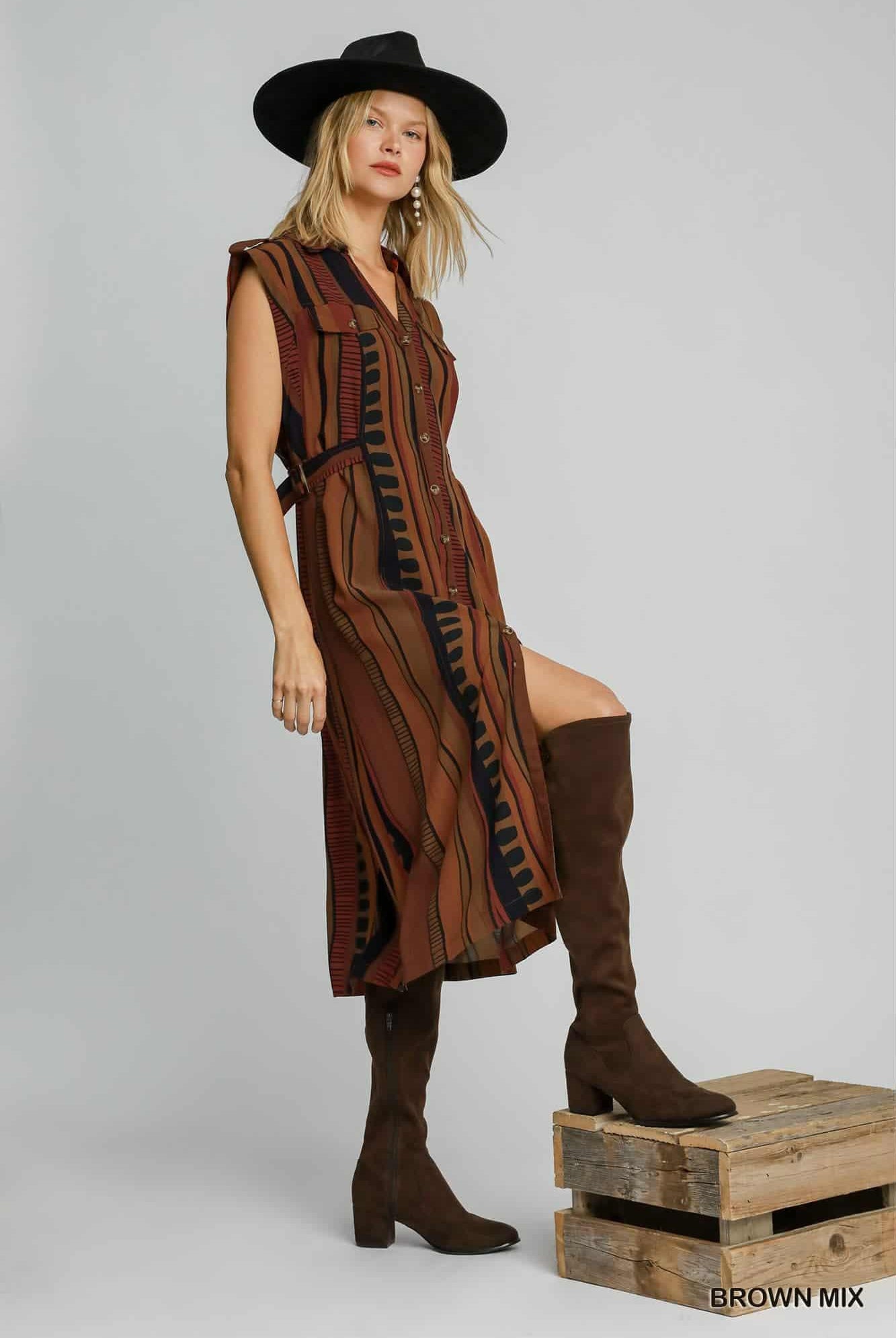 Woman wearing a brown dress and boots on a wooden crate against a gray background