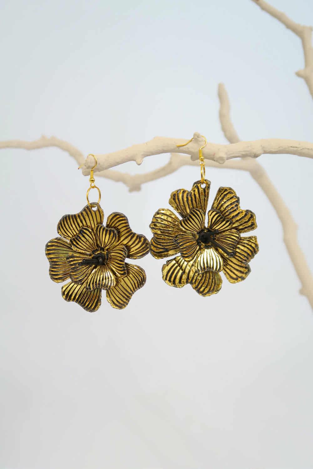 Pair of gold floral earrings on a branch with a light background