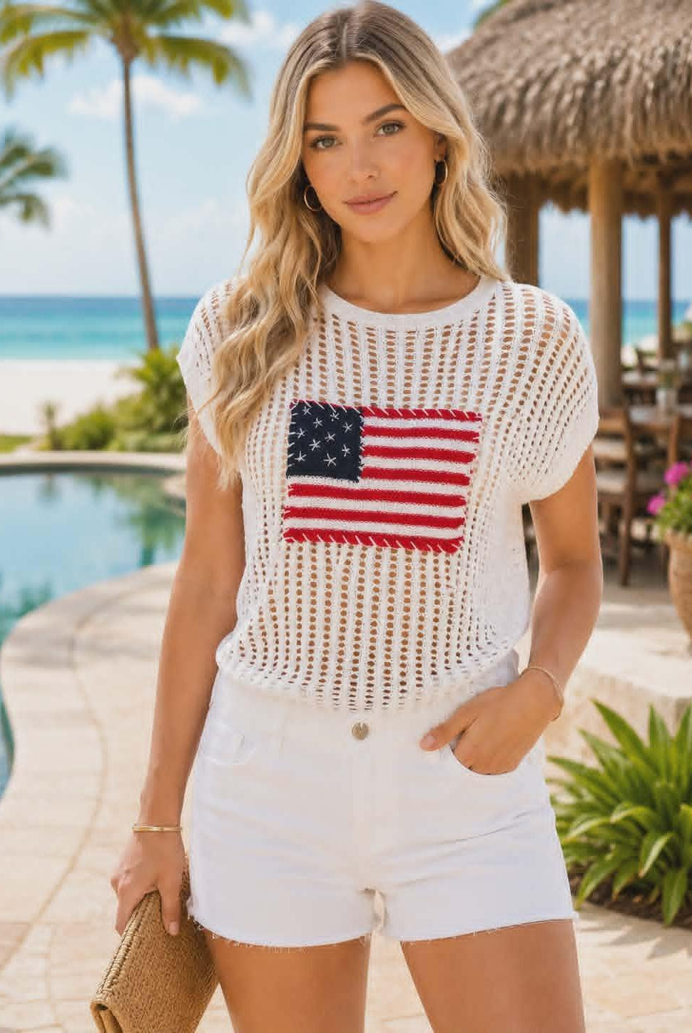 Beautiful resort chic model wearing a lightweight white crochet sweater with an American flag detail and white shorts at a tropical beach resort.