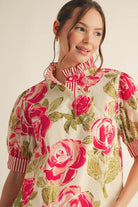 Model wearing bold rose floral blouse with striped collar and puff sleeves