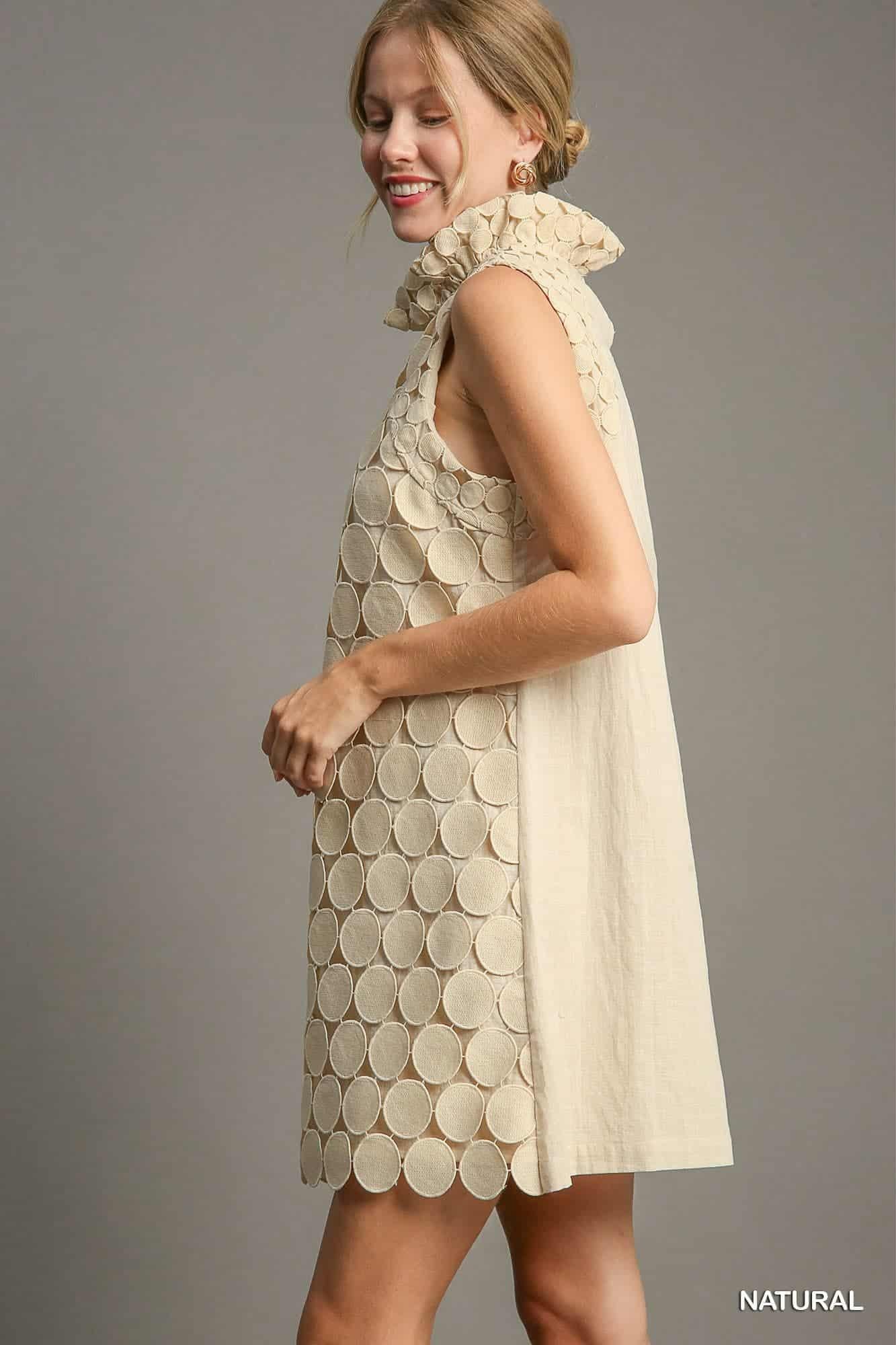 Woman wearing a beige sleeveless dress with circular pattern on a gray background, SIDE VIEW