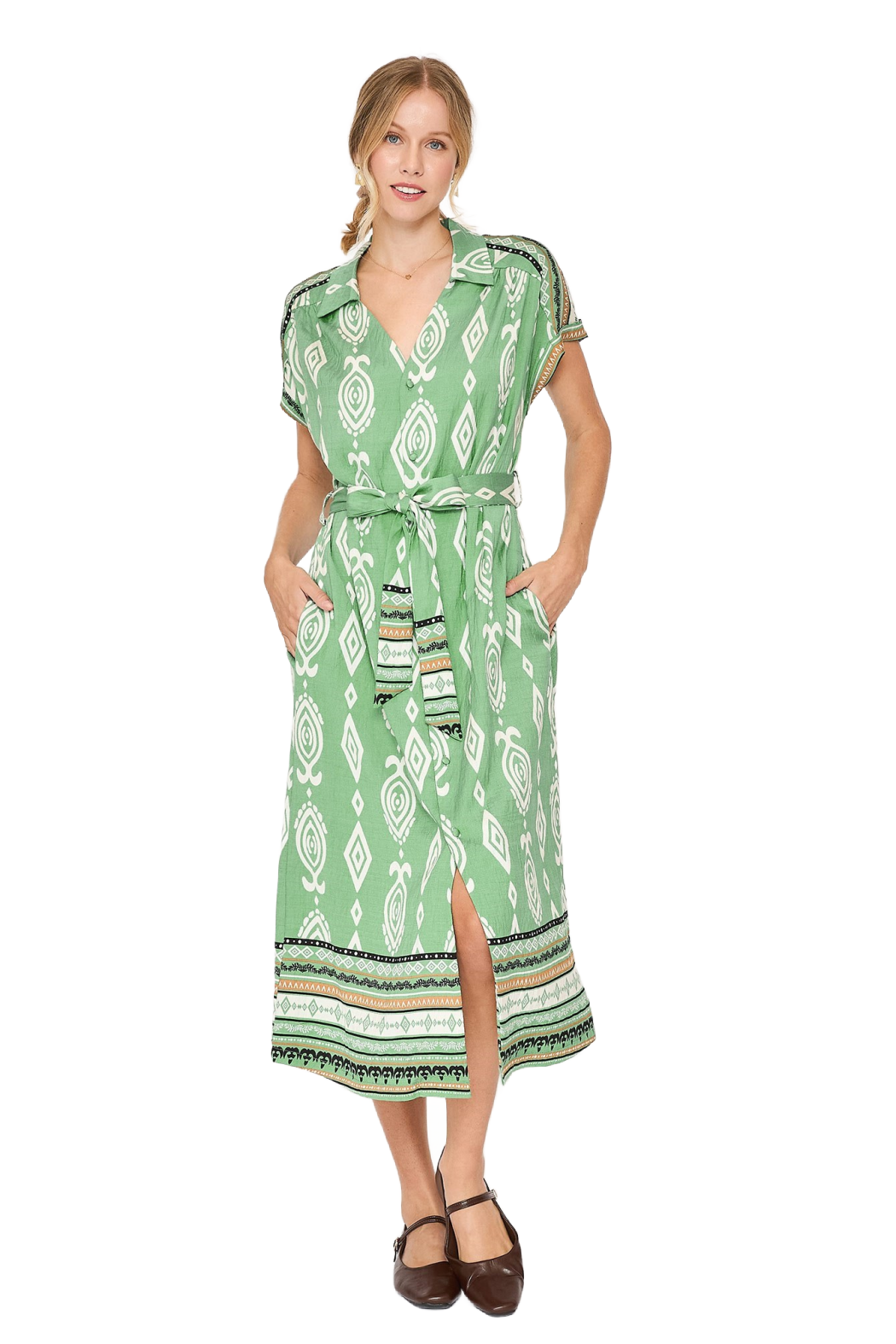 A woman modeling a light green short-sleeve midi dress with a white geometric pattern, a tie waist belt, and side pockets, paired with brown flat shoes against a plain white background.