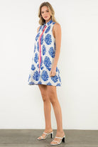 Woman wearing a sleeveless dress with blue floral pattern against a white background