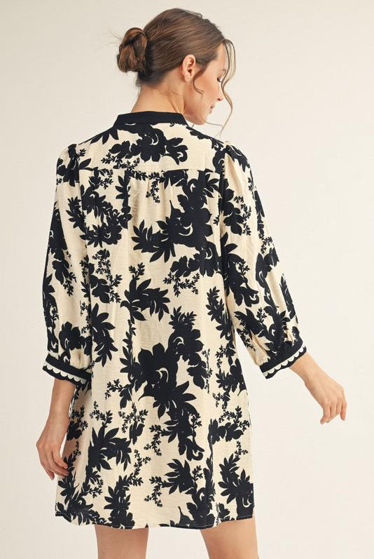 Model wearing Jodifl black and cream floral tunic dress with scalloped trim neckline and ¾ sleeves, back view, photographed against white background— Petunias of Naples