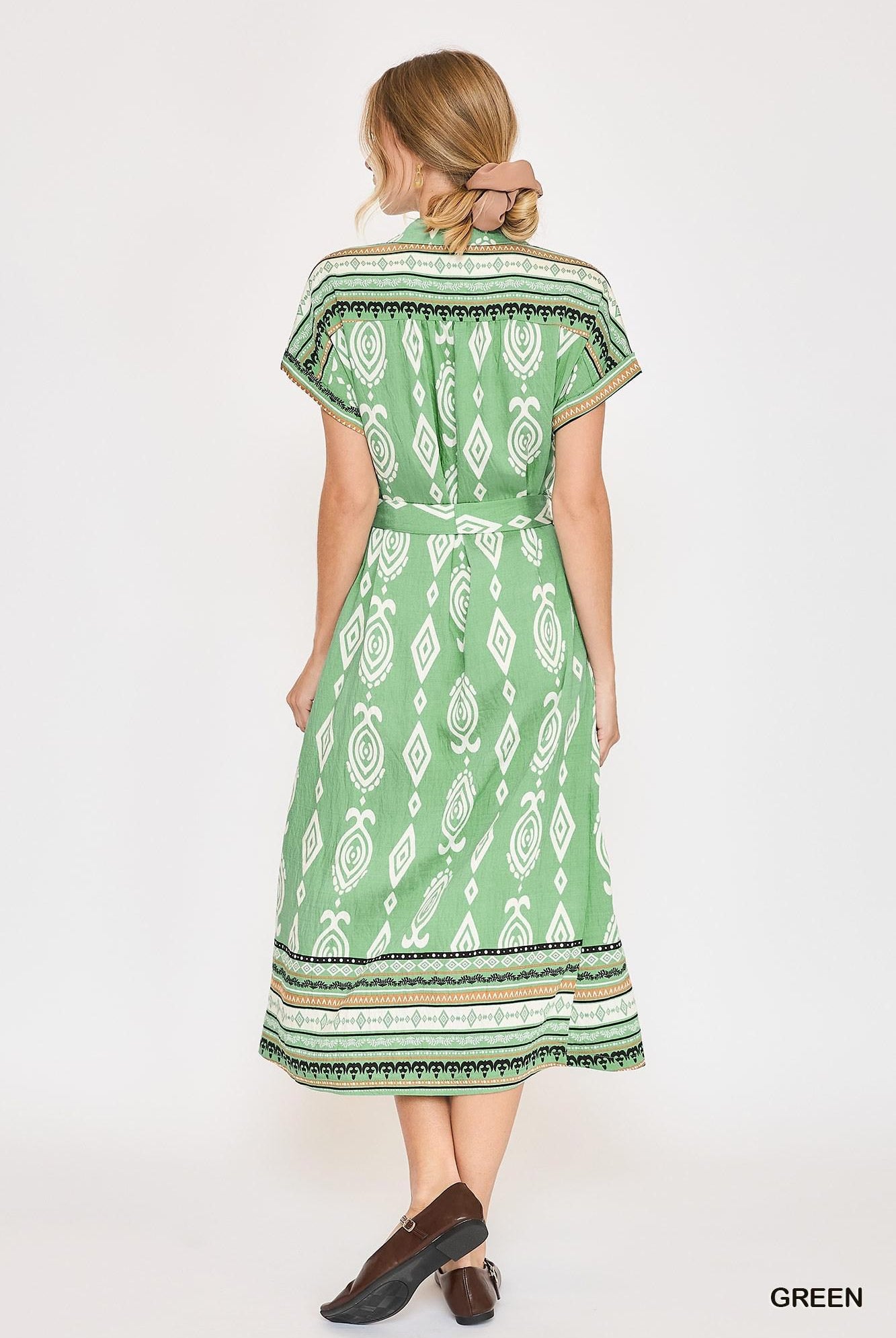 A woman shown from the back wearing a green midi dress with a white geometric pattern and a matching waist tie, paired with brown shoes, against a plain white background.