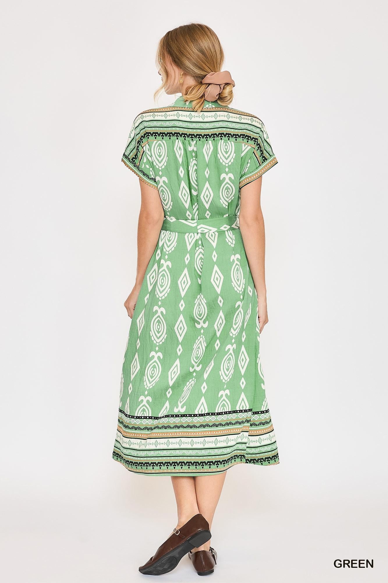 A woman shown from the back wearing a green midi dress with a white geometric pattern and a matching waist tie, paired with brown shoes, against a plain white background.