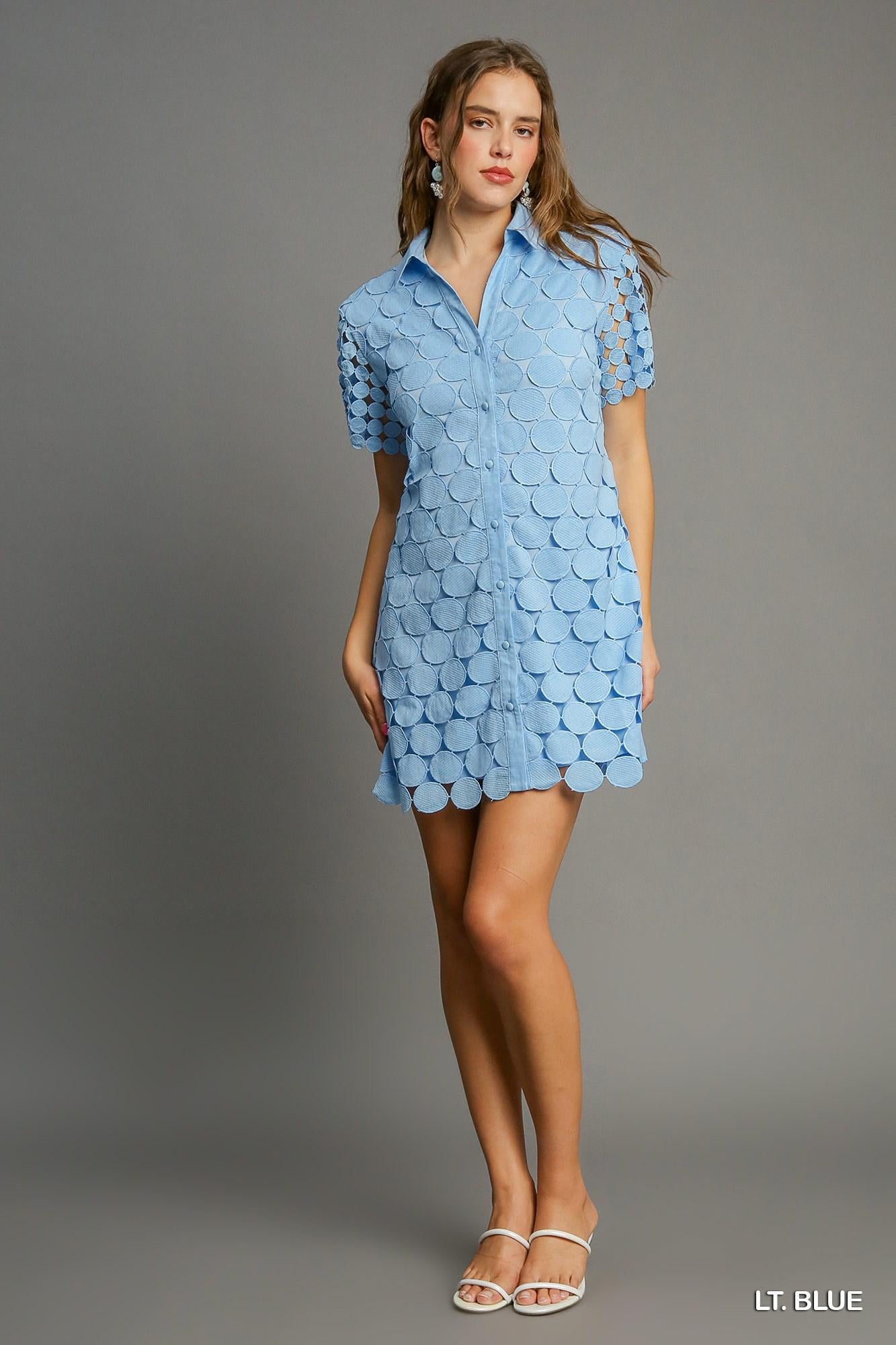 Model wearing light blue shirt dress with circular appliqué detailing and short sleeves, styled with white sandals.