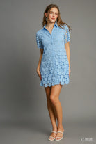 Model wearing light blue shirt dress with circular appliqué detailing and short sleeves, styled with white sandals.