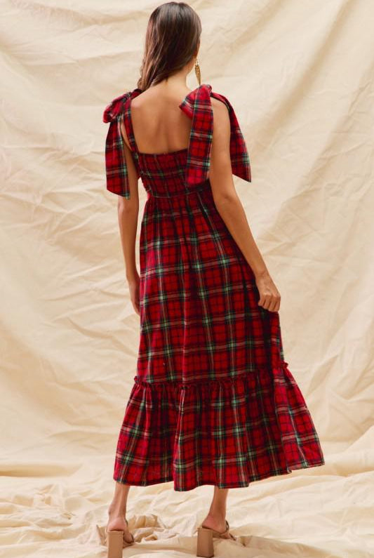 Woman wearing a red plaid dress with a beige background, back View