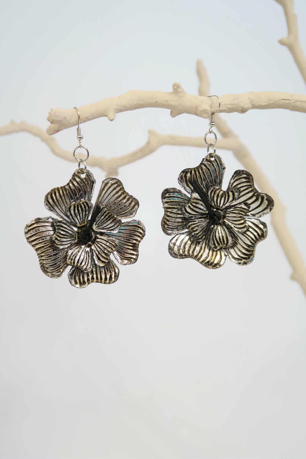 Floral silver earrings hanging on a branch with a white background