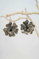 Floral silver earrings hanging on a branch with a white background