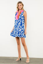 Woman wearing a blue patterned dress with pink accents against a white background