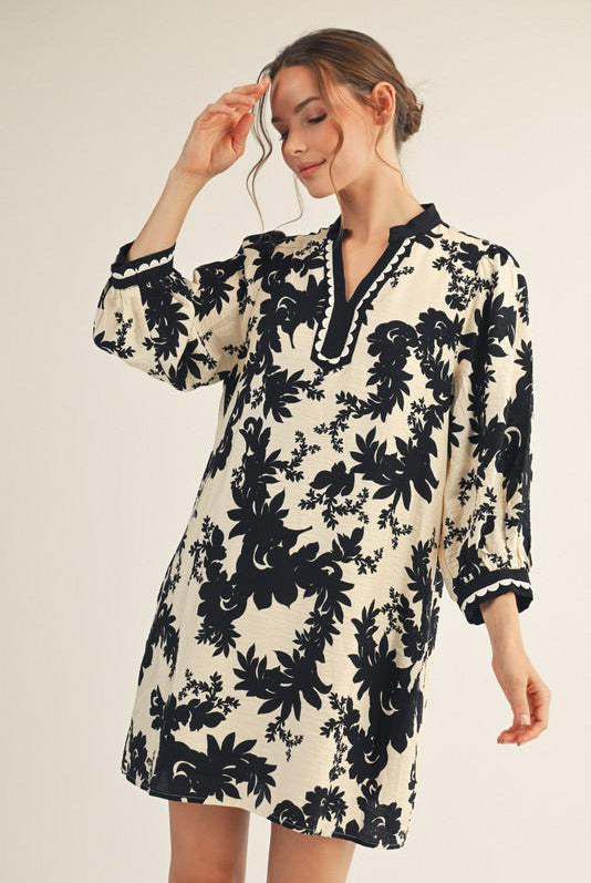 Model wearing Jodifl black and cream floral tunic dress with scalloped trim neckline and ¾ sleeves, photographed against white background— Petunias of Naples