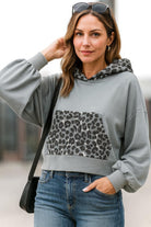 . Urban chic woman wearing a gray hoodie with leopard print pocket and hood, styled with jeans.
