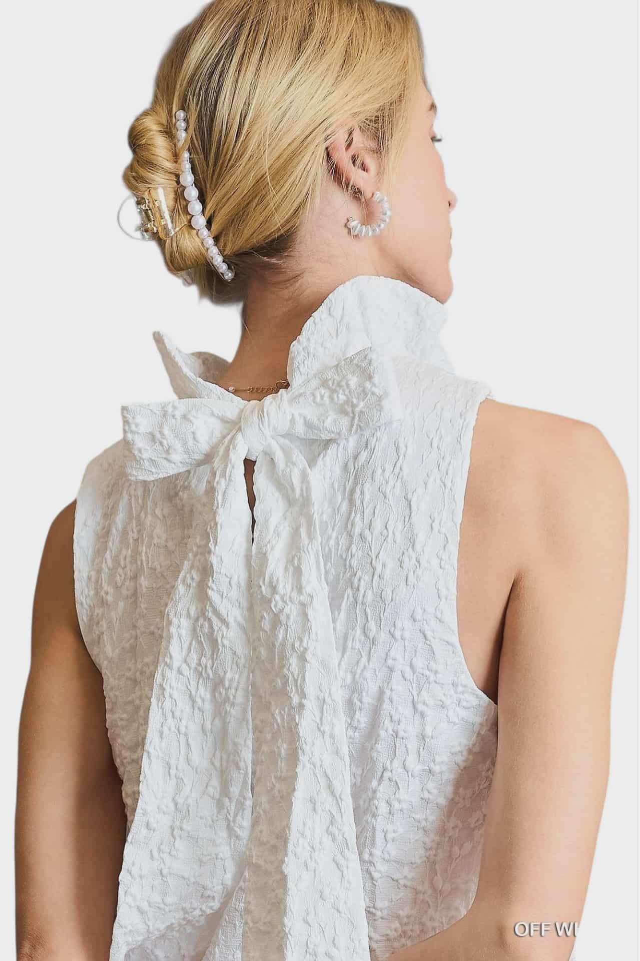 Back view of white sleeveless dress featuring an oversized bow at the neckline.