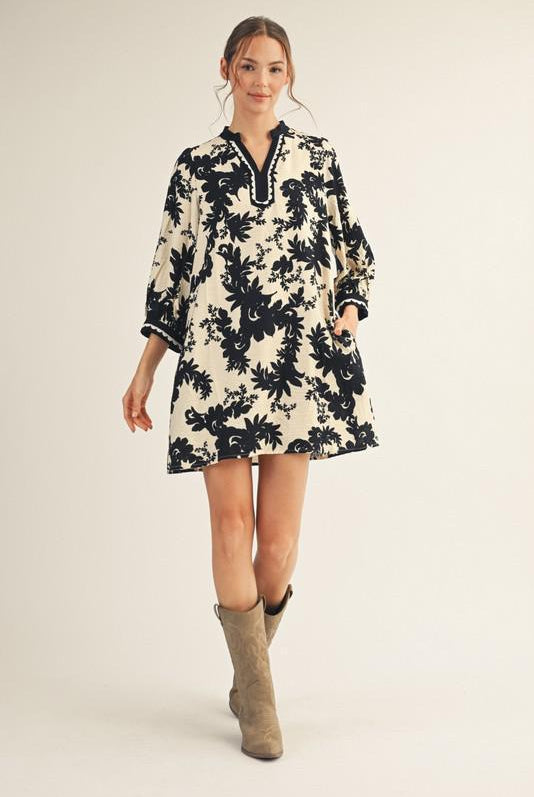 Model wearing Jodifl black and cream floral tunic dress with scalloped trim neckline and ¾ sleeves, photographed against white background— Petunias of Naples
