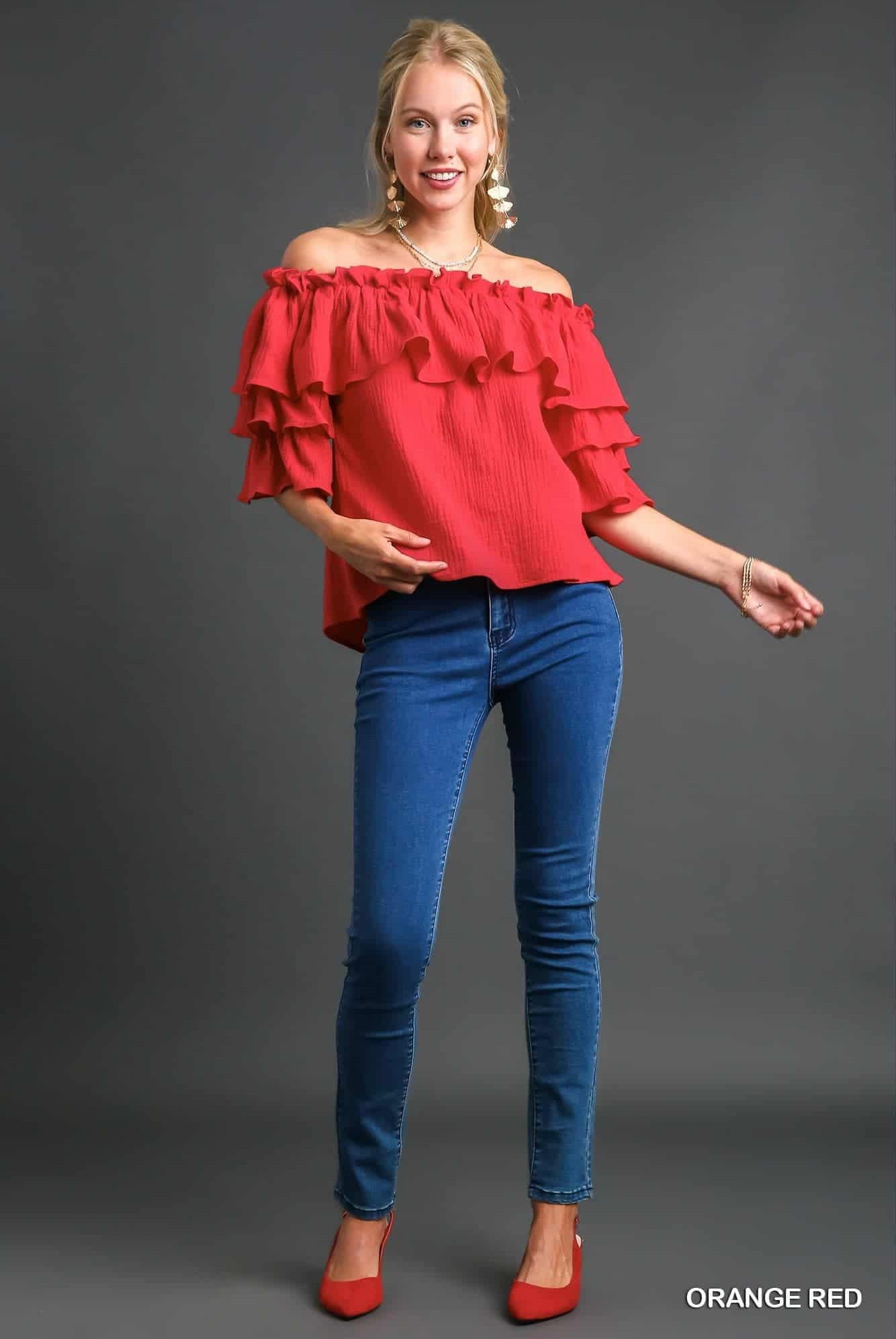 Woman wearing a red off-shoulder top and blue jeans on a gray background