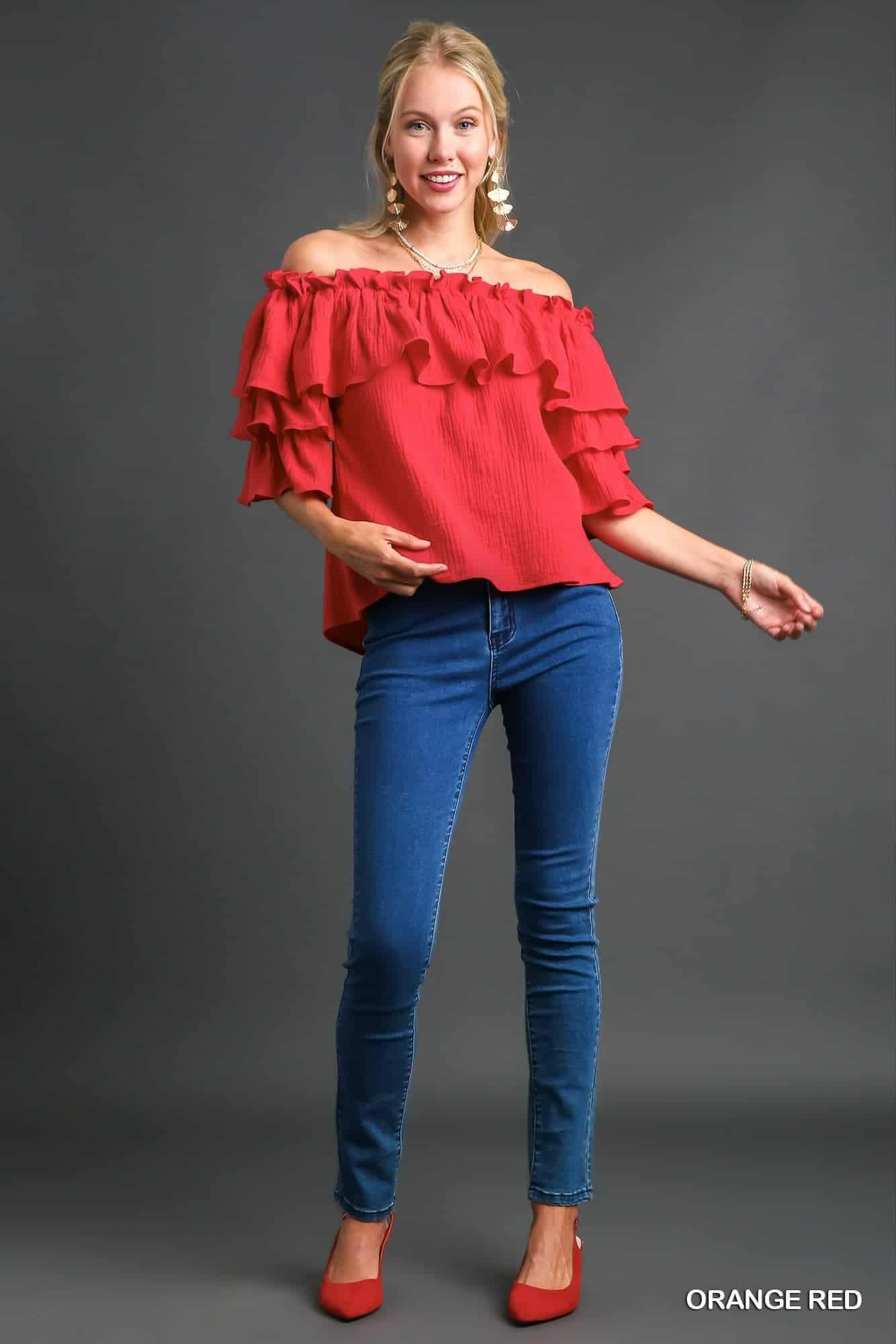 Woman wearing a red off-shoulder top and blue jeans on a gray background