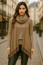 Beautiful urban chic woman wearing an taupe sweater with attached vest and fringe hem, styled with leather pants on a city street.