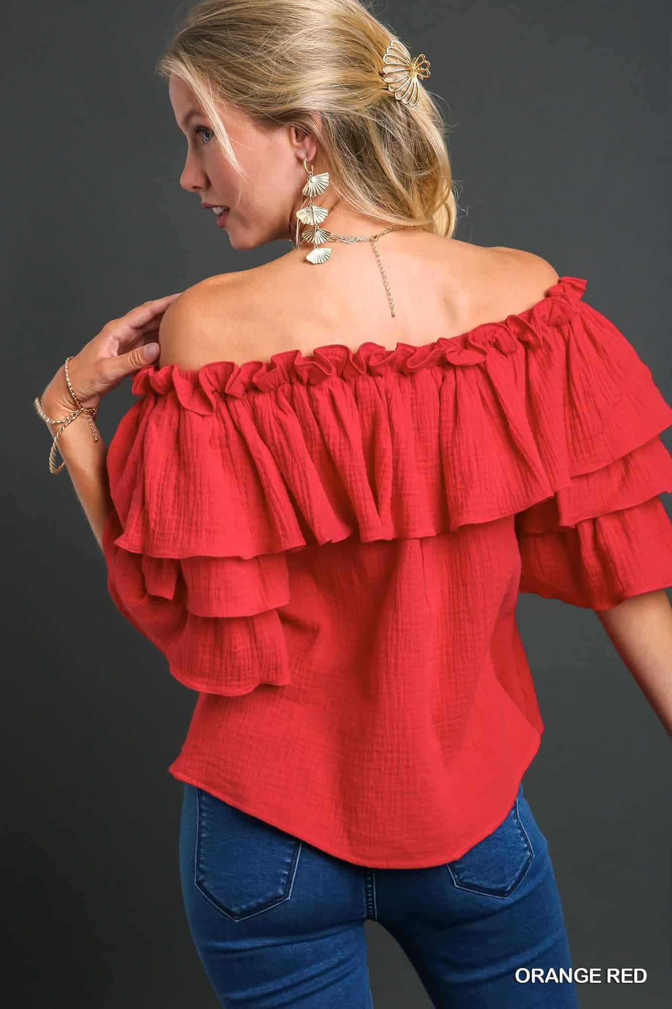 Woman wearing a red off-shoulder top with ruffled layers on a dark background, back view