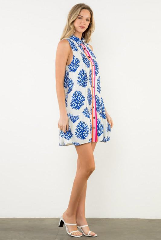 Woman wearing a sleeveless dress with a blue floral pattern on a white background, sideview