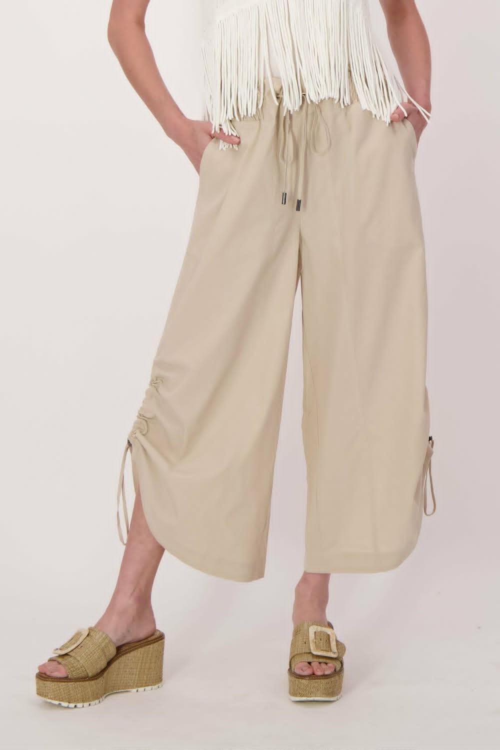 Person wearing beige wide-leg pants with a white top and sandals on a light background