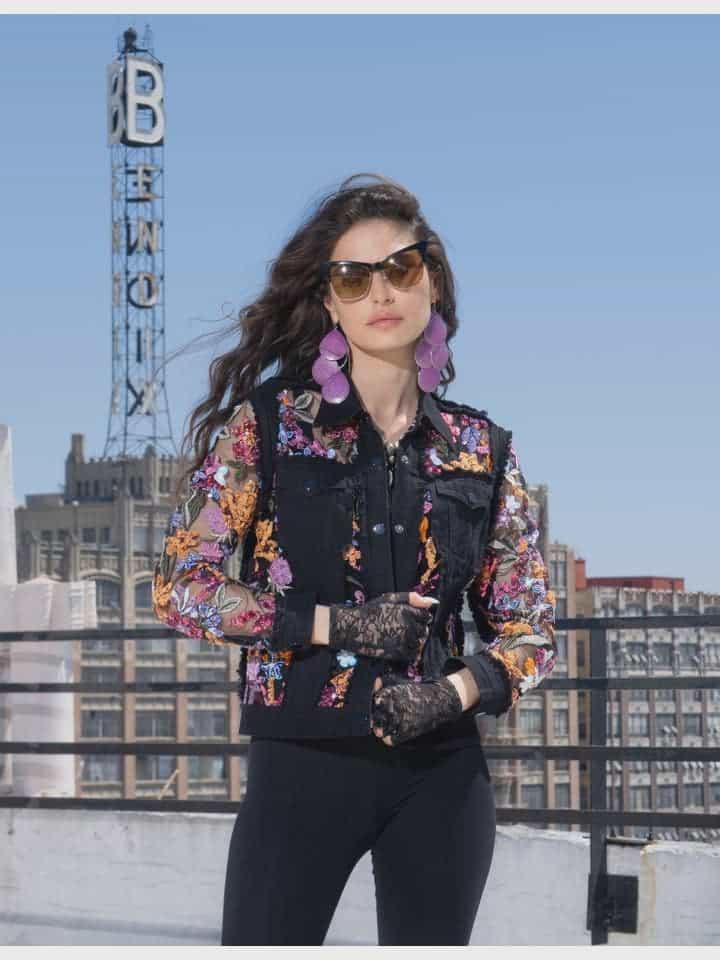 Woman wearing a colorful sequin embroidered floral black jacket on a rooftop with cityscape background