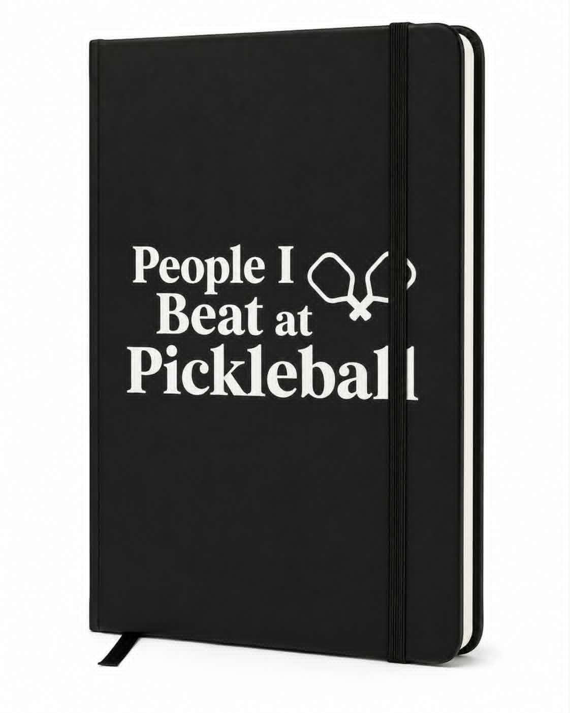 Black hardcover journal with "People I Beat at Pickleball" printed in white lettering, featuring pickleball paddle graphics, an elastic closure, and ribbon bookmark.