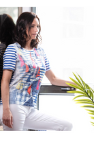 Woman wearing a colorful striped shirt sitting at a desk with a plant in the foreground.