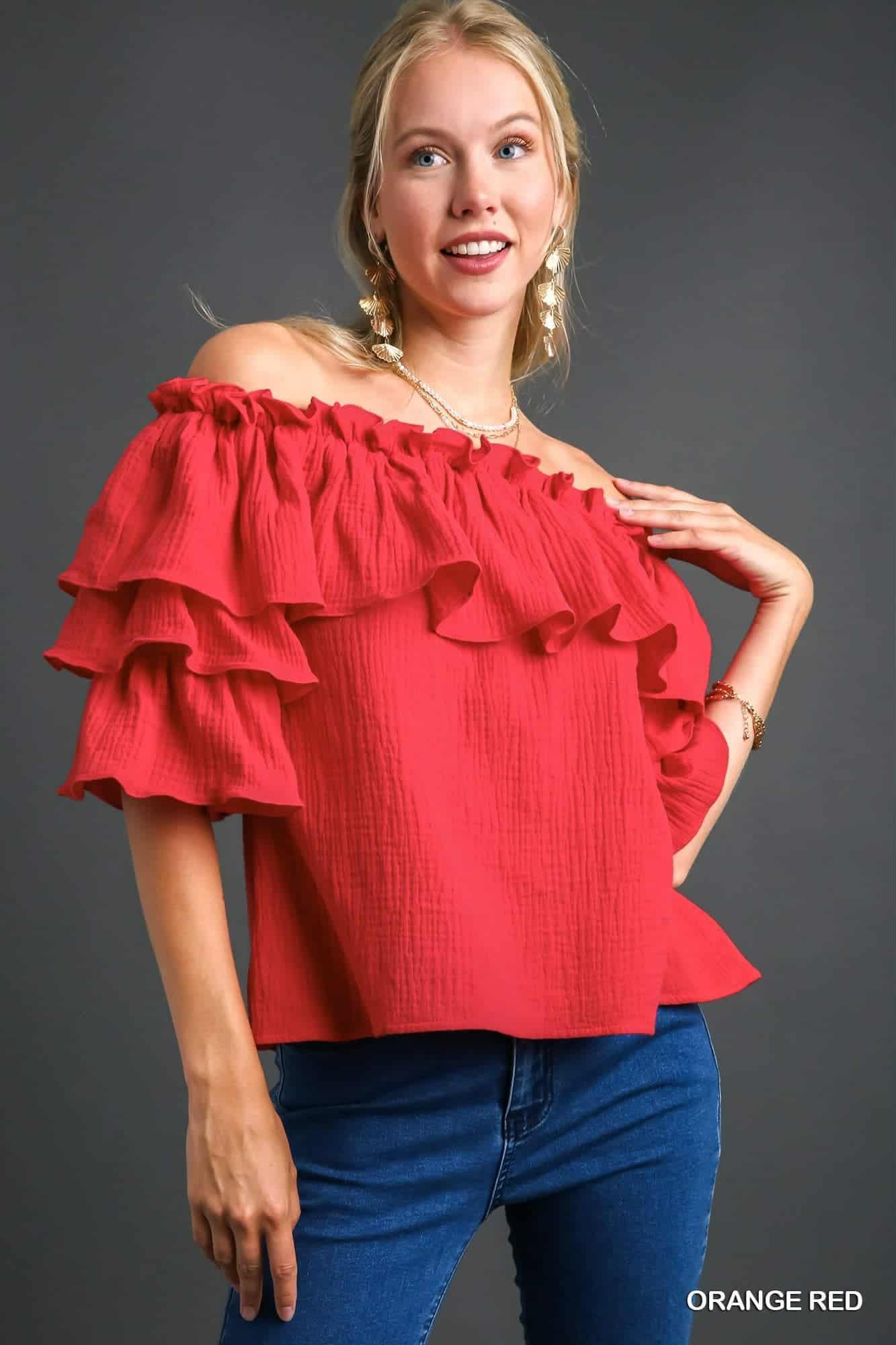 Woman wearing a red off-shoulder top with ruffles on a gray background