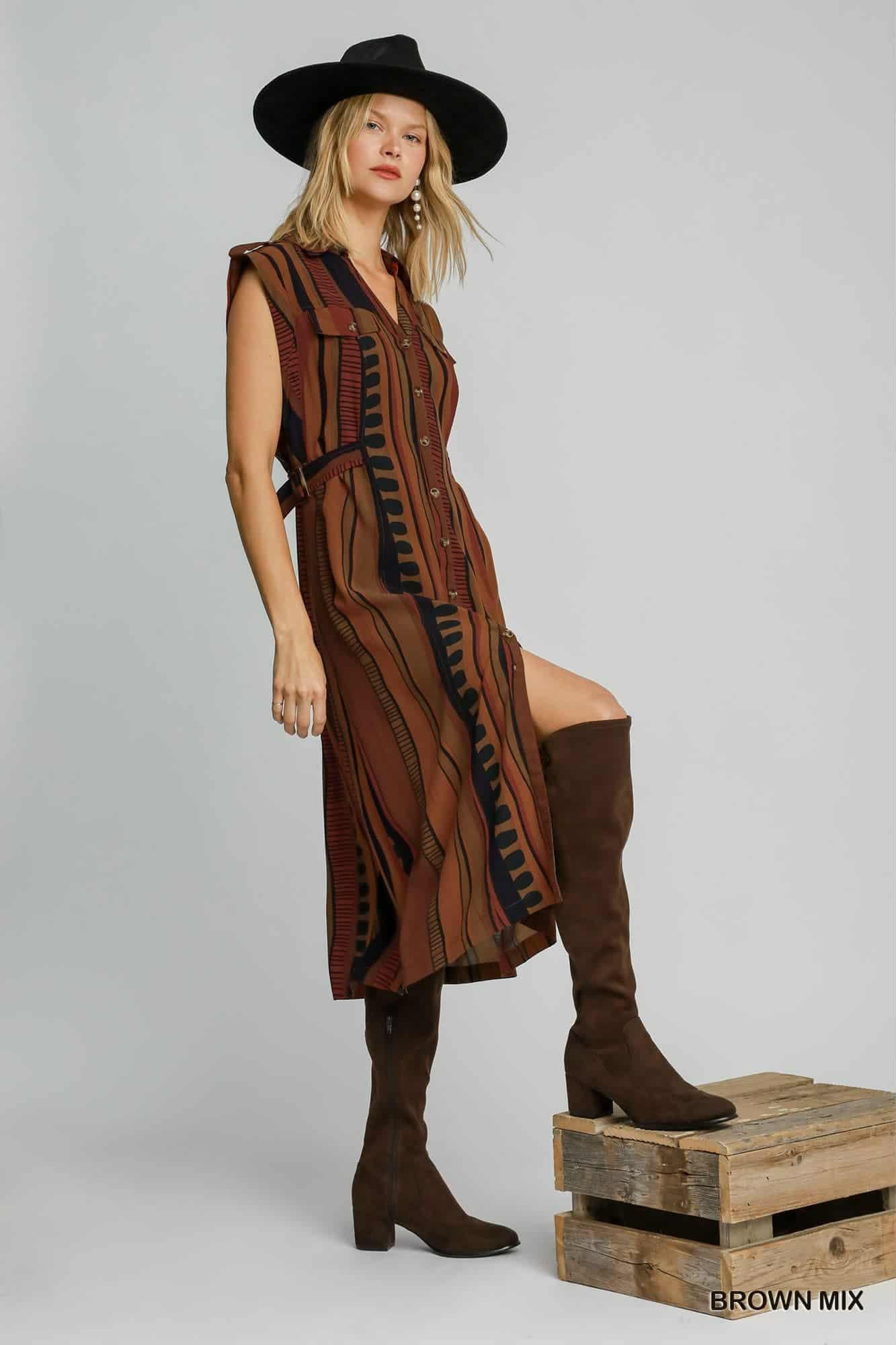 Woman wearing a brown dress and boots on a wooden crate against a gray background