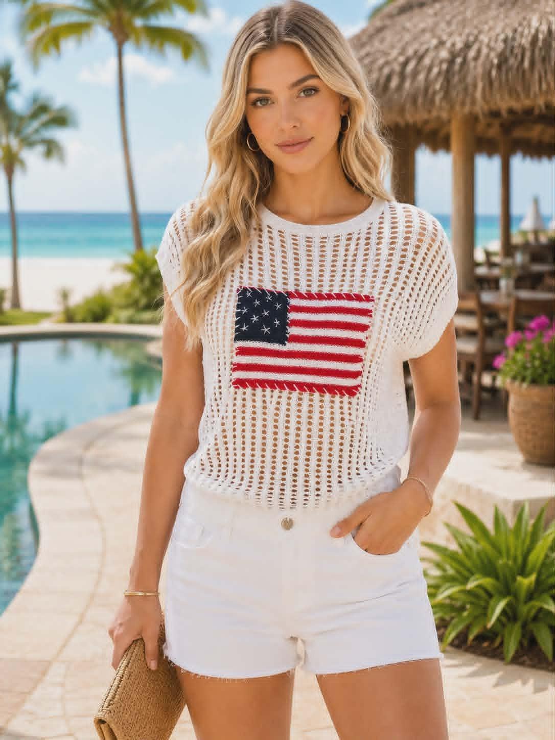 Beautiful resort chic model wearing a lightweight white crochet sweater with an American flag detail and white shorts at a tropical beach resort.