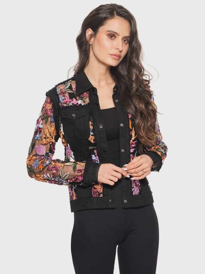 Woman wearing a black denim jacket with floral  sequins and embroidery on a white background