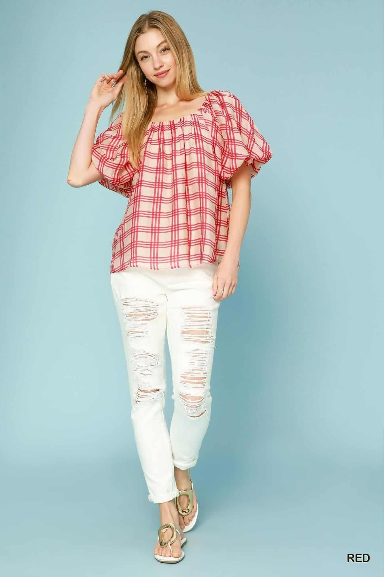 Beautiful woman wearing a red plaid peasant blouse with puff sleeves and white jeans, styled in an urban street background.

