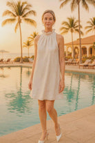 Model wearing a sleeveless white textured dress with ruffled neckline and A-line silhouette.