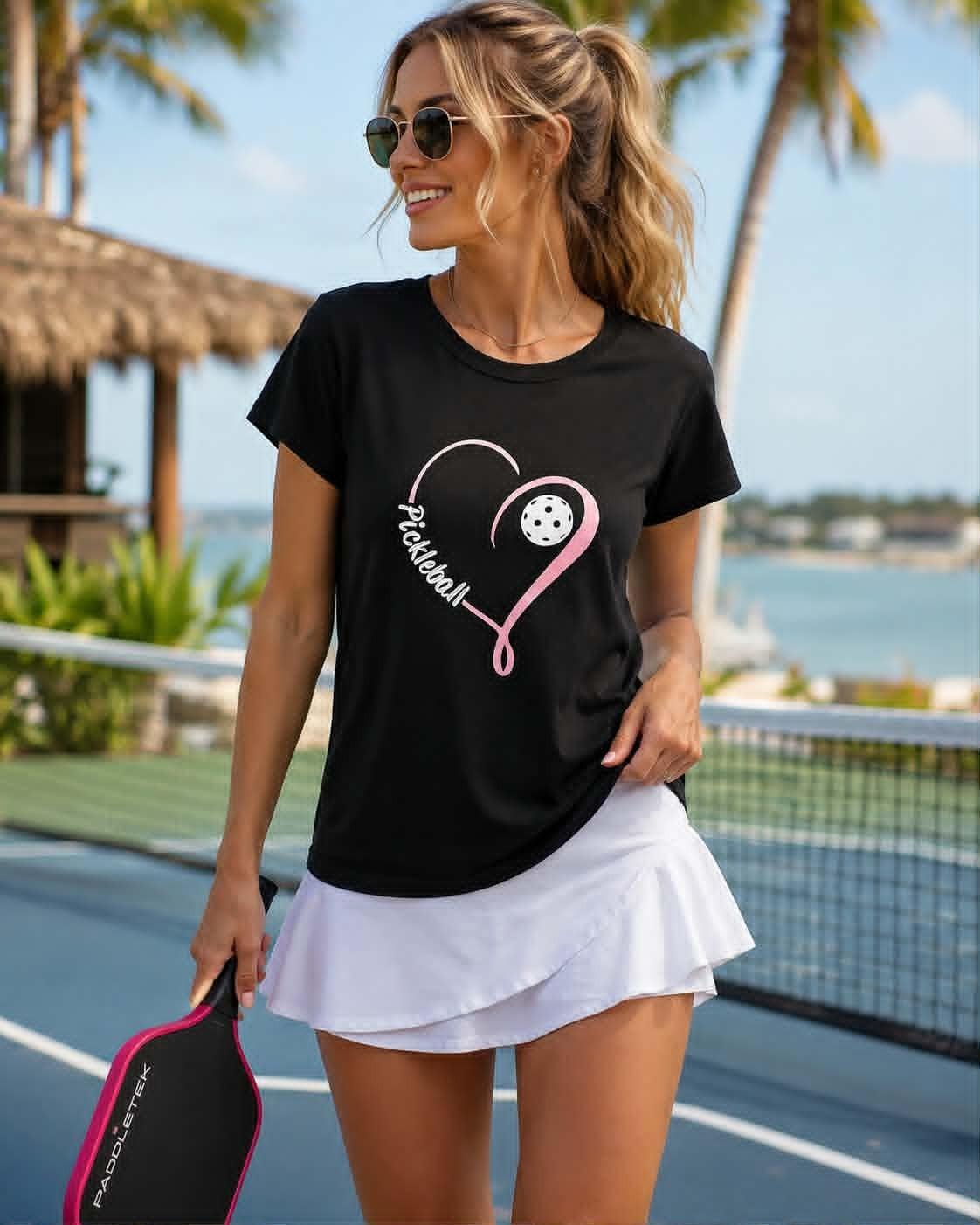 Women's black poly-spandex crew neck tee featuring a pink heart pickleball graphic, styled for casual resort-chic and pickleball-inspired fashion