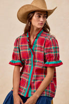 Woman wearing red plaid blouse with green trim and ruffled puff sleeves – festive holiday top by Petunias of Naples