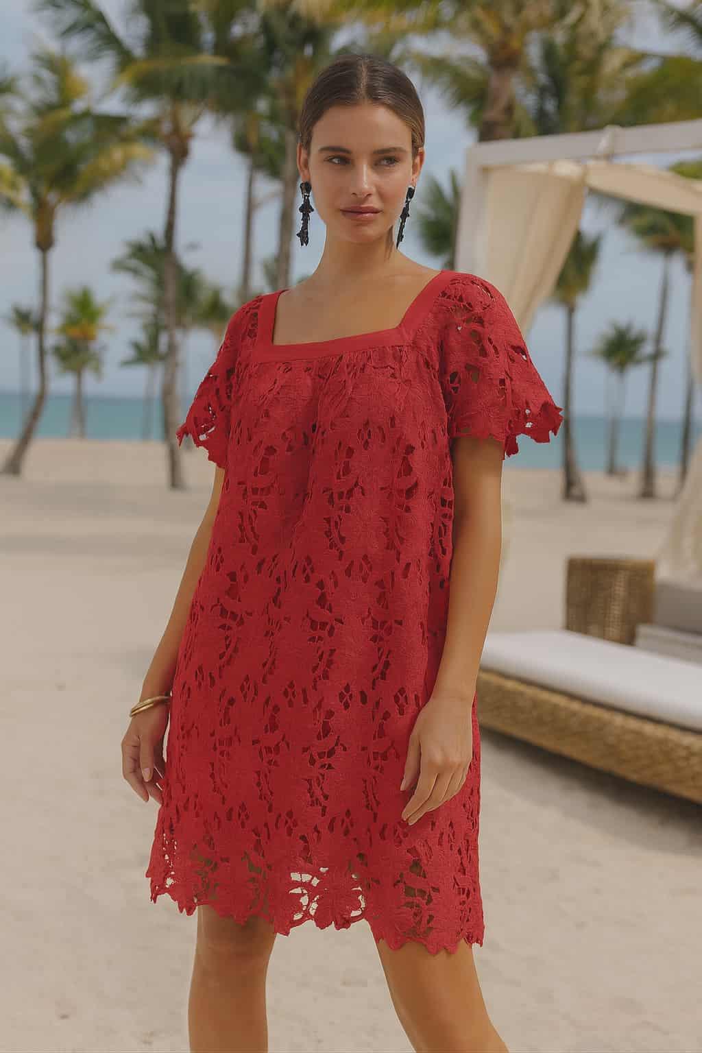 Woman wearing a coral rose lace shift dress with floral cutwork design, short sleeves, and a square neckline in a tropical resort setting.