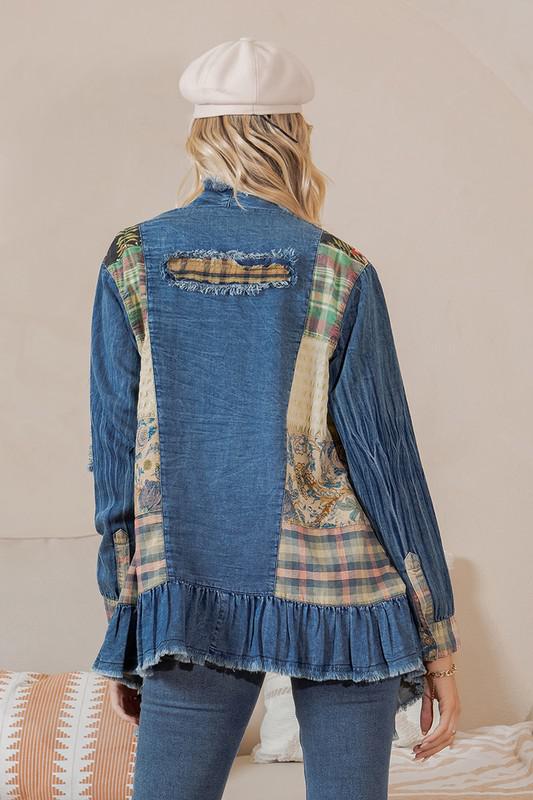 Person wearing a blue denim jacket with patches and a white cap, standing against a neutral background.