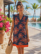 Woman wearing navy floral Voy resort dress with coral tropical print and ruffle sleeves at a luxury beach resort.
