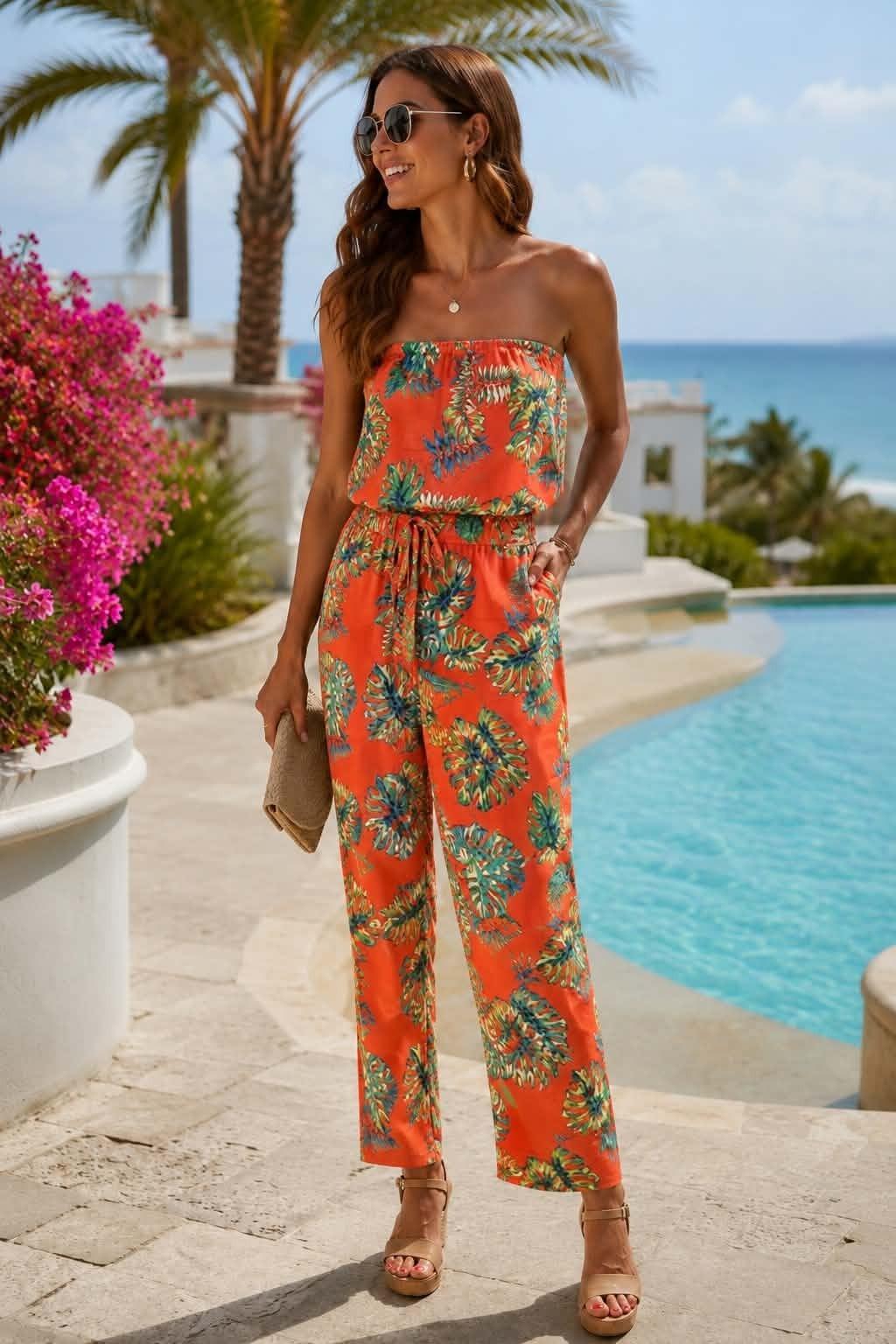 Women's coral strapless tropical print jumpsuit featuring a vibrant leaf pattern, elastic waist with self-tie belt, and relaxed straight-leg silhouette.