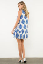 Woman wearing a sleeveless dress with blue floral pattern on a white background, backview