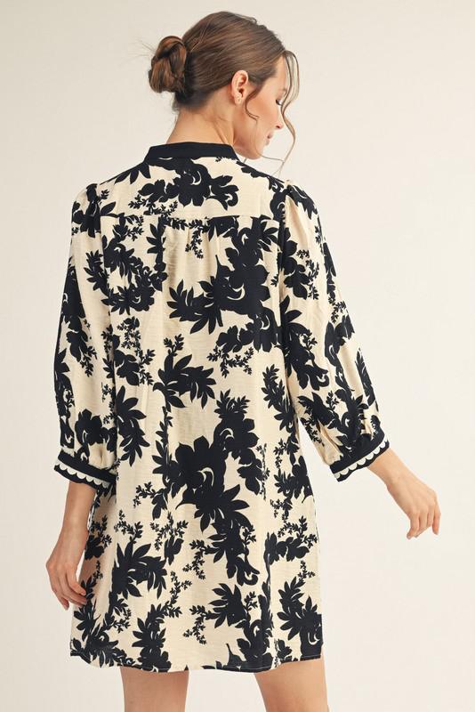 Model wearing Jodifl black and cream floral tunic dress with scalloped trim neckline and ¾ sleeves, back view, photographed against white background— Petunias of Naples