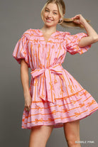 Woman wearing an Umgee pink dress with orange patterns on a gray background