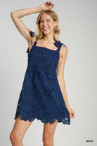 Woman wearing an Umgee navy lace dress on a gray background