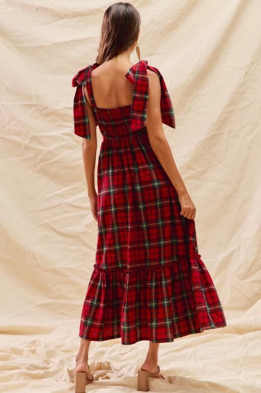Woman wearing a red plaid dress with a beige background, back View