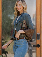 Woman wearing a denim jacket with patterned sleeves and jeans standing in front of a wooden door.